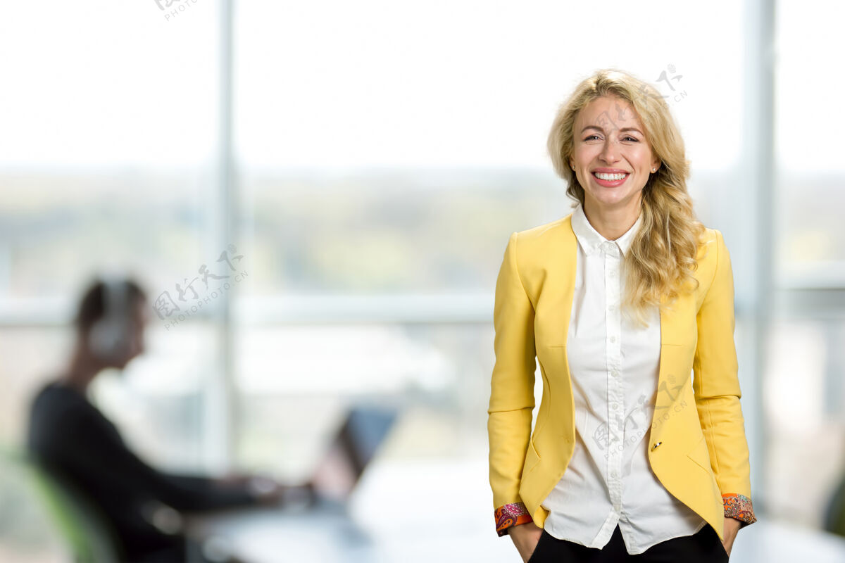 快乐美丽的年轻女商人的画像微笑着站在办公室窗户上快乐的年轻经理愉悦女士积极