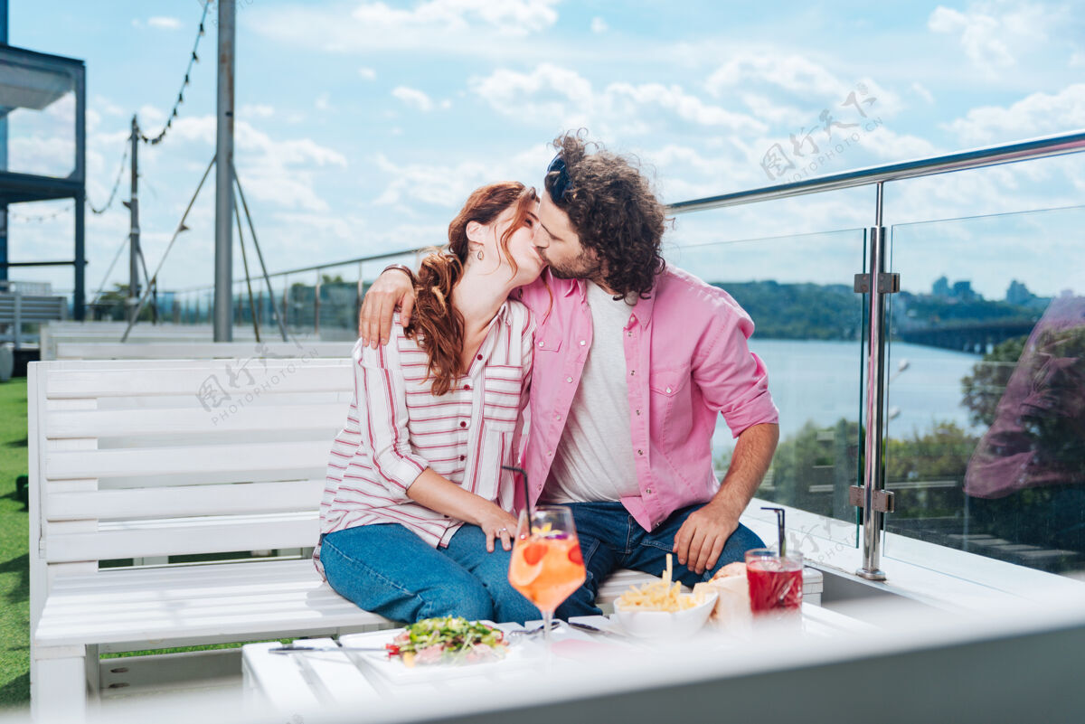 晚餐未来的妻子卷曲胡须的男人亲吻他未来的妻子在美丽的夏日露台上吃浪漫的晚餐男性空气关系