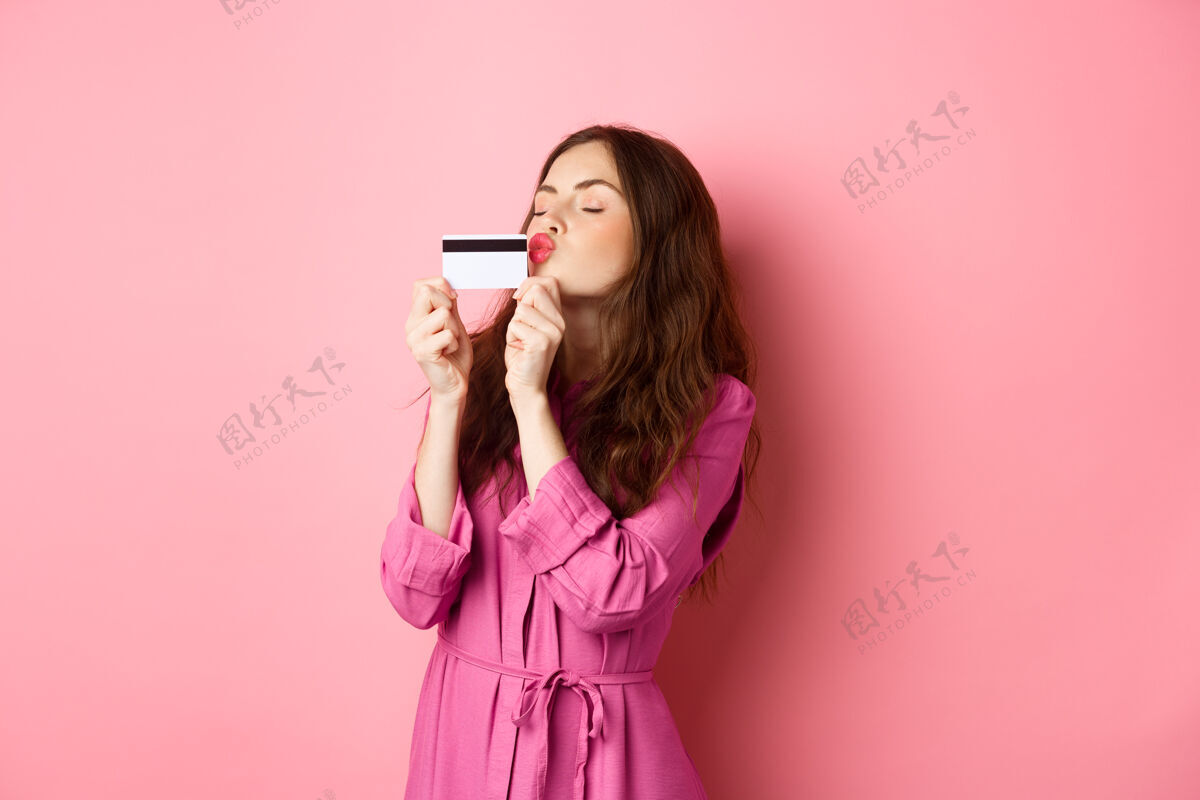 快乐年轻漂亮的女人亲吻她的信用卡 去购物 在商店里浪费钱 站在粉红色的墙上复制空间乐观快乐休闲