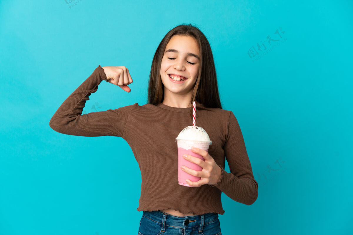 手势小女孩拿着草莓奶昔孤立在蓝色背景上做着强烈的手势牛奶小提神