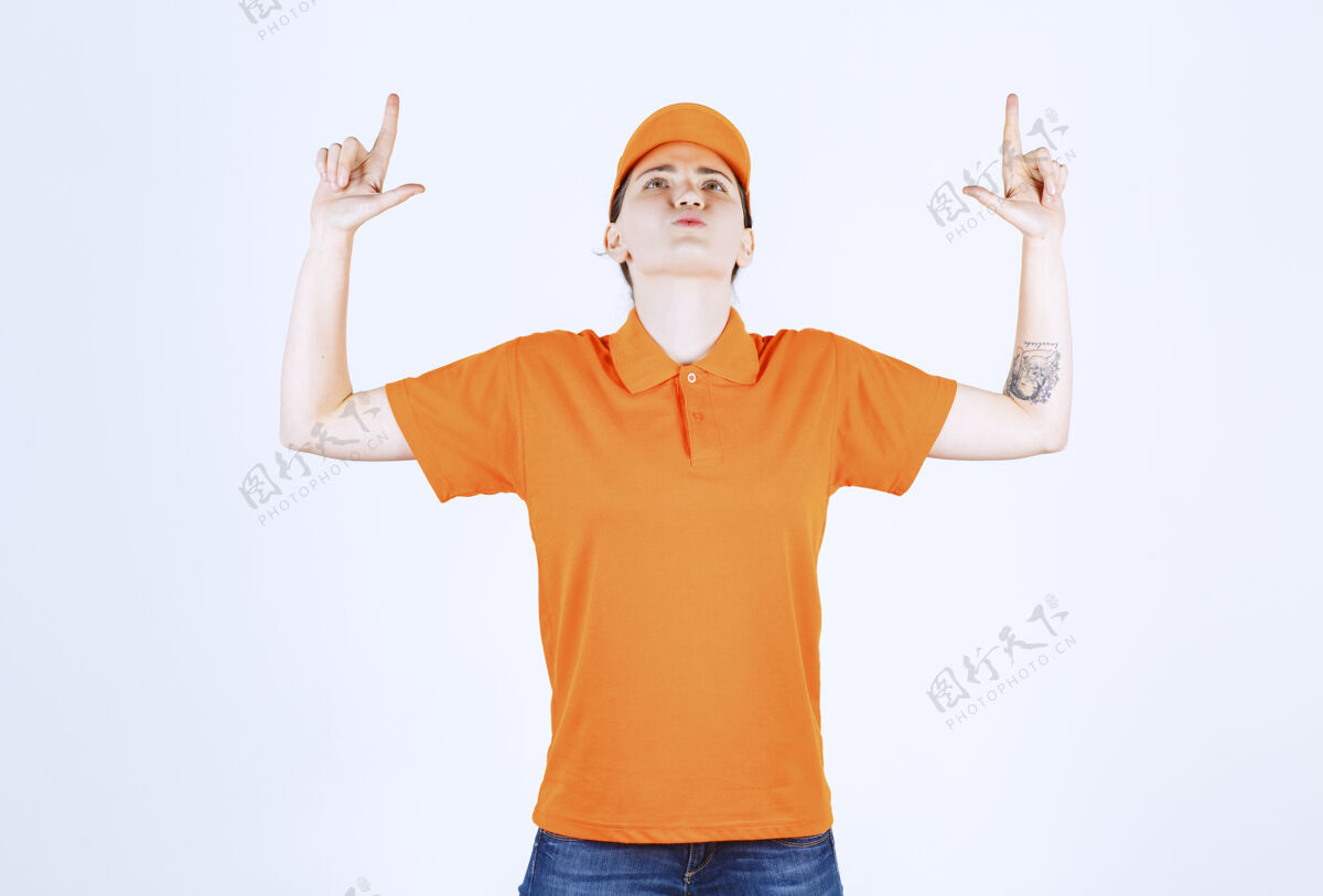 漂亮身着橙色衬衫的女青年信使一边抬头 一边向上指年轻女人年轻年轻女人