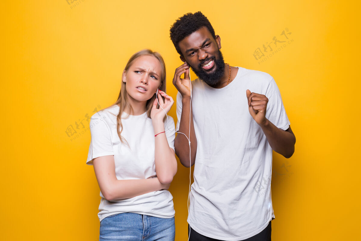 现代一对快乐的夫妇一边唱歌 一边用智能手机和耳机隔着黄色的墙一起唱歌欢呼基本惊人