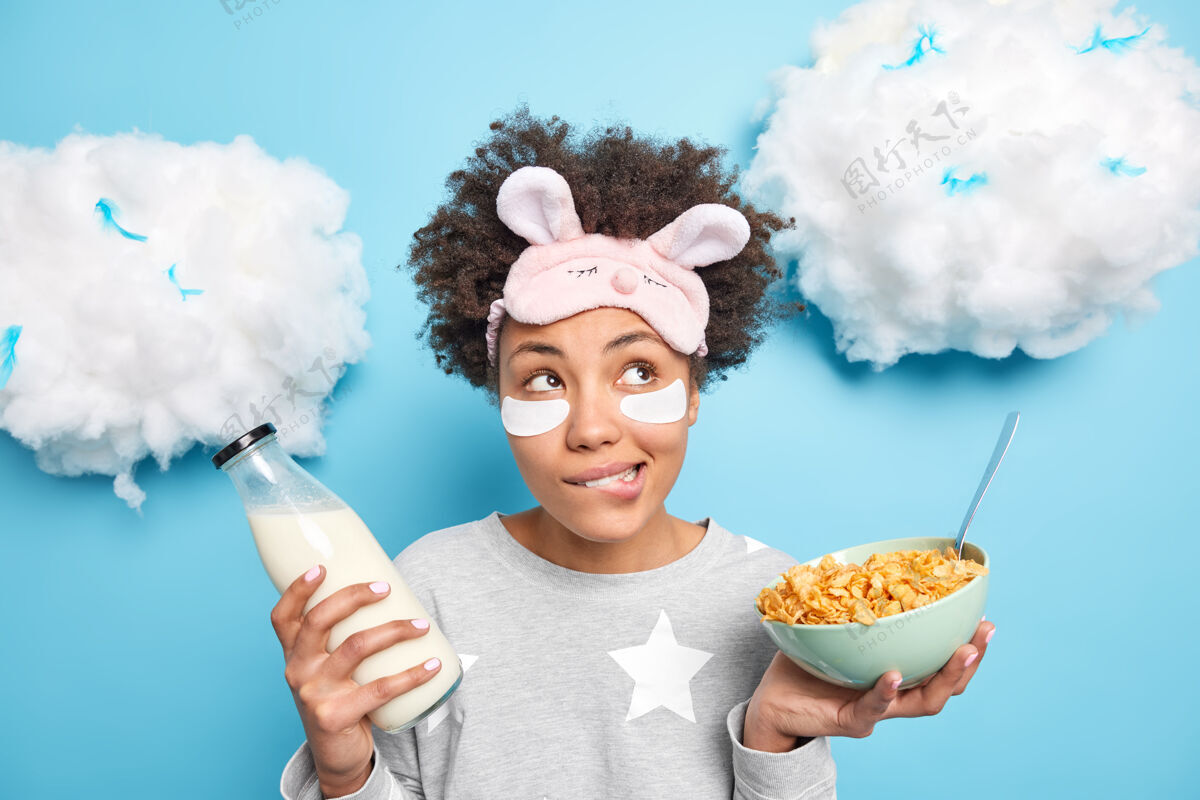 垫女人咬嘴唇去吃早餐拿着一碗麦片和奶瓶穿睡衣在眼睛下面贴上眼罩去除蓝色隔离的皱纹咬人膳食