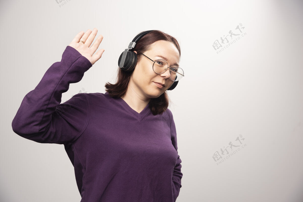 站立戴着眼镜的年轻女子戴着耳机在听音乐 这是一张高质量的白色照片青春肖像姿势