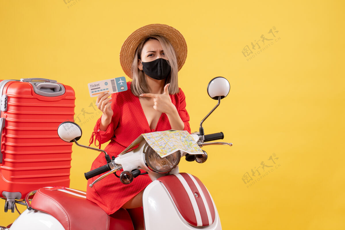 摩托车正面图：骑着轻便摩托车的年轻女士拿着大箱子 手里拿着票度假摩托车冒险