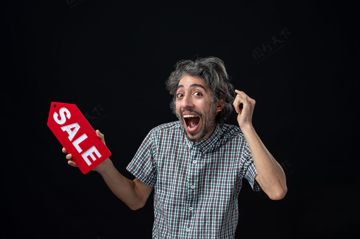 脸正面图滑稽开朗的男子举着黑色墙上的红色销售标志观点人性感