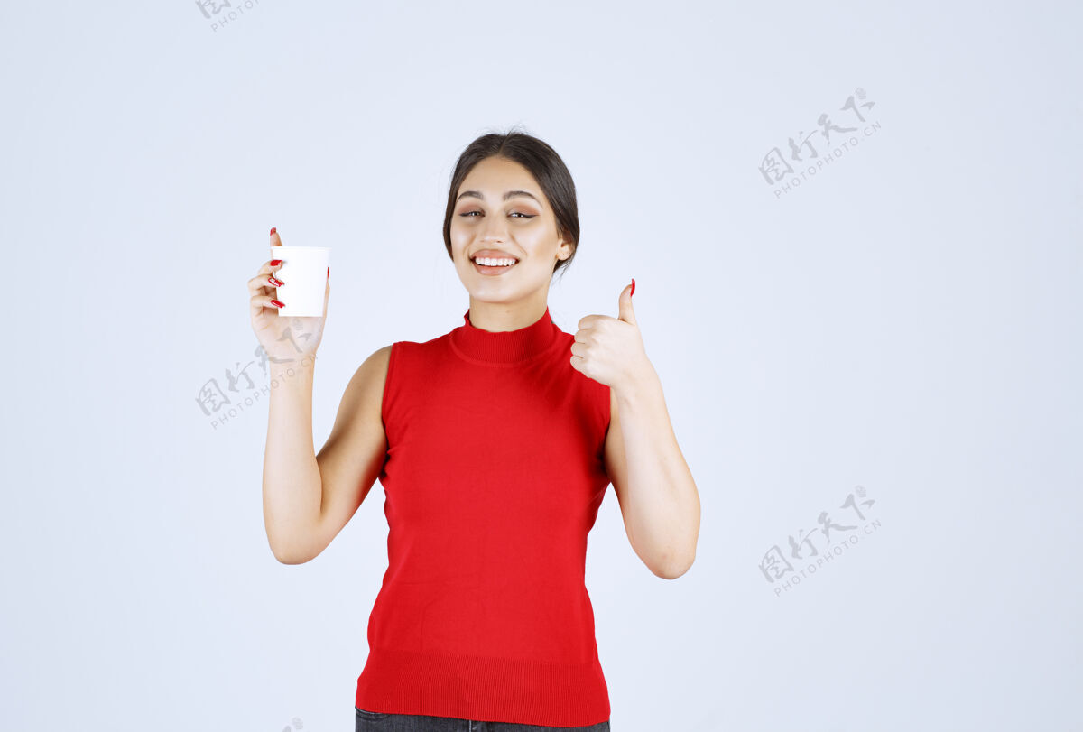 模特穿红衬衫的女孩在喝咖啡 并表现出积极的迹象美味女性员工