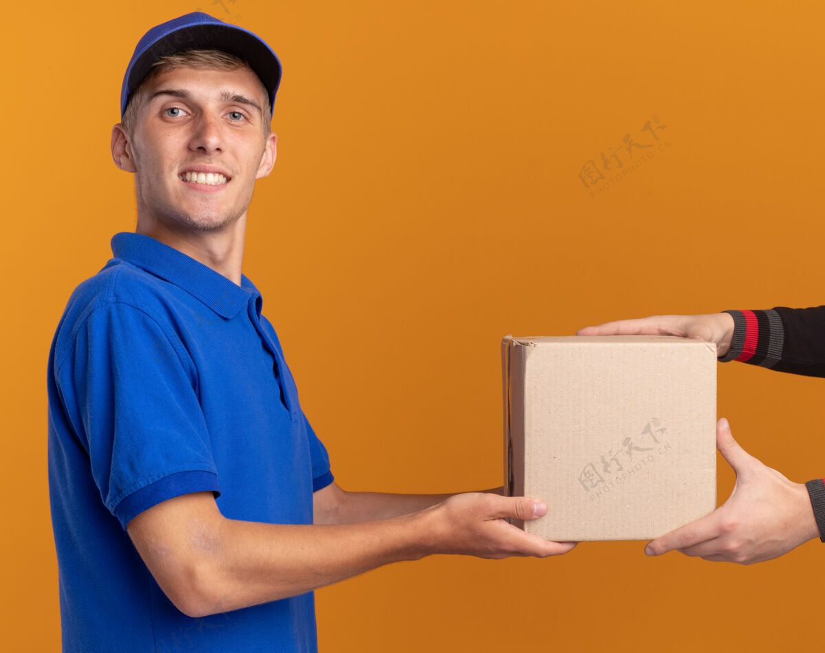 金发微笑着的年轻金发送货员站在一旁 把名片盒递给看着相机的人给予侧身站着