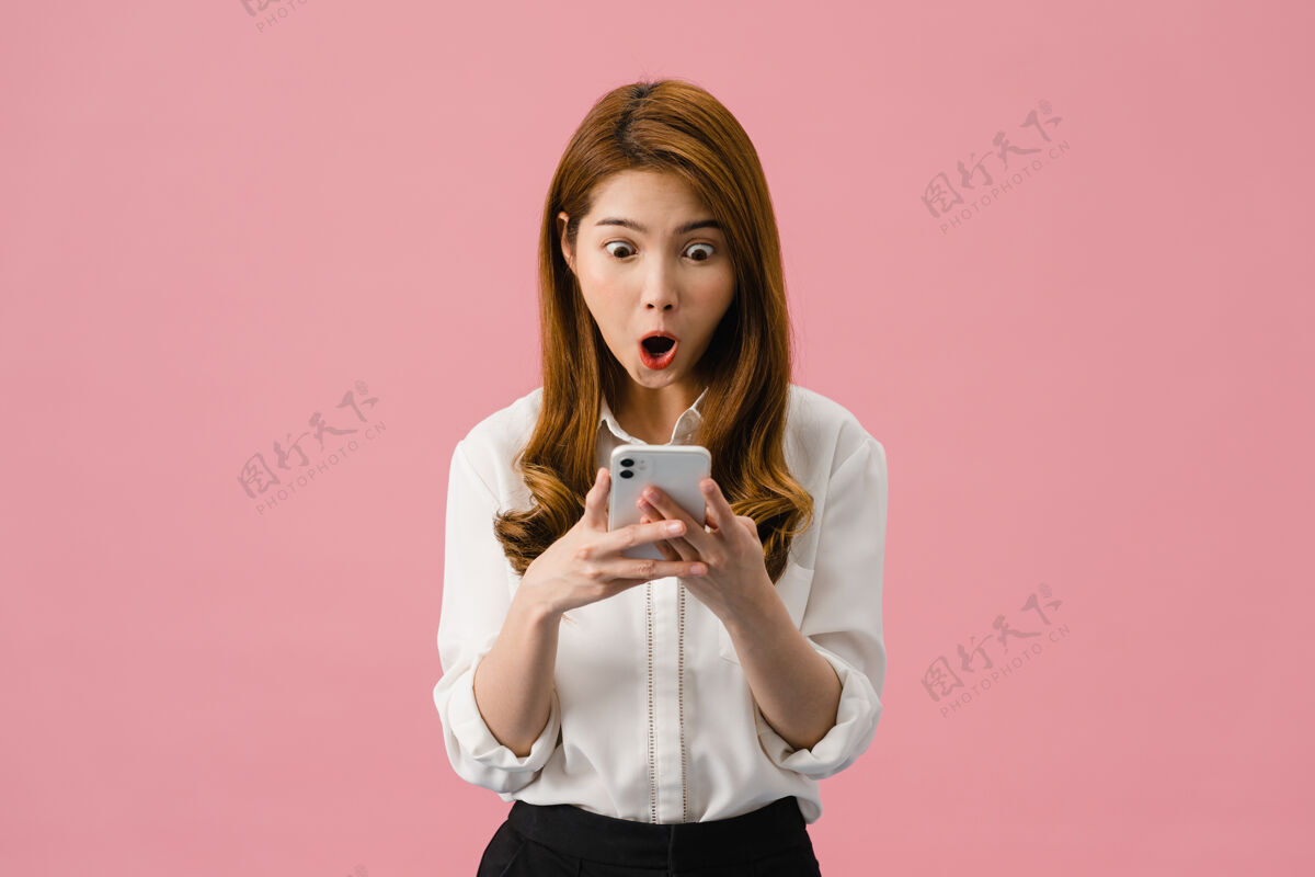 专业人士年轻的亚洲女士用手机 表情积极 笑容灿烂 穿着休闲服 感觉幸福 孤立地站在粉色背景上休闲女性电话