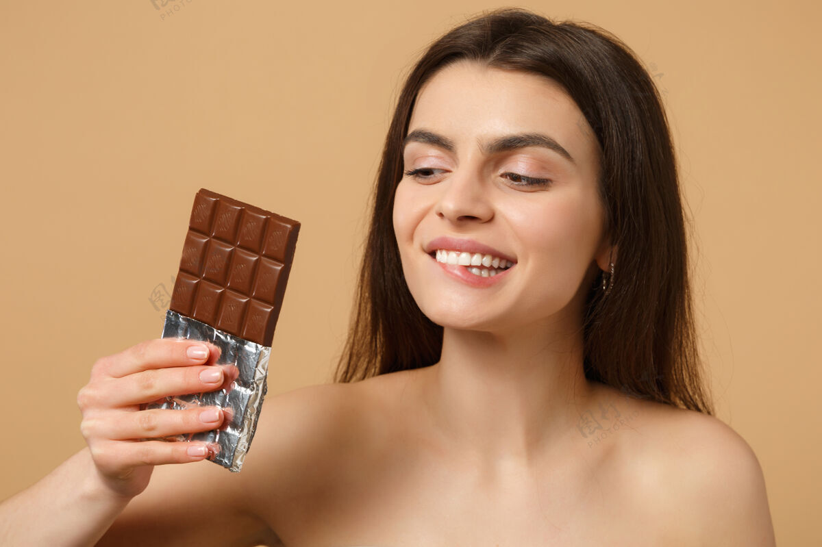 不健康近距离拍摄完美肌肤的半裸女人 裸妆将巧克力棒隔离在米色粉彩墙上感官饮食健康
