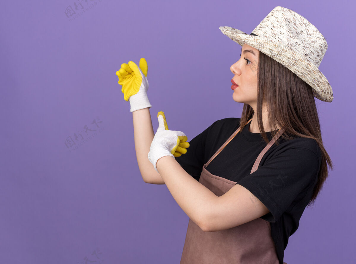 指向焦急漂亮的白人女园丁戴着园艺帽和手套指着后面看一边背部紫色帽子