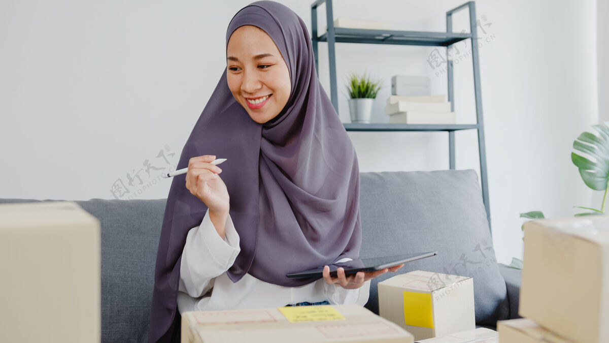 电子商务年轻的穆斯林女商人检查产品采购订单的库存和保存到平板电脑工作在家办公印尼语卖家头巾