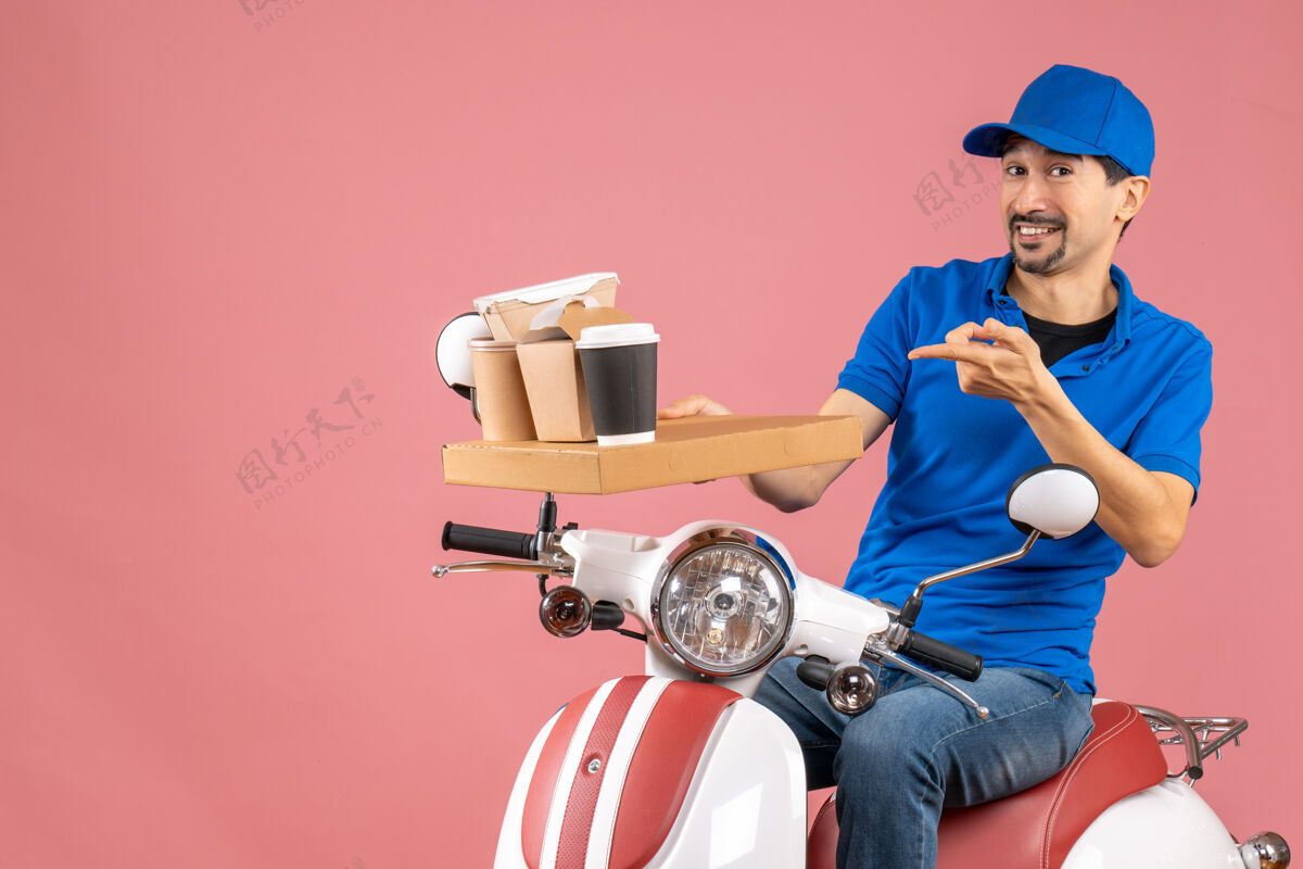 快递员满意的快递员戴着帽子坐在粉彩桃色背景上的滑板车上的俯视图背景卡通粉彩