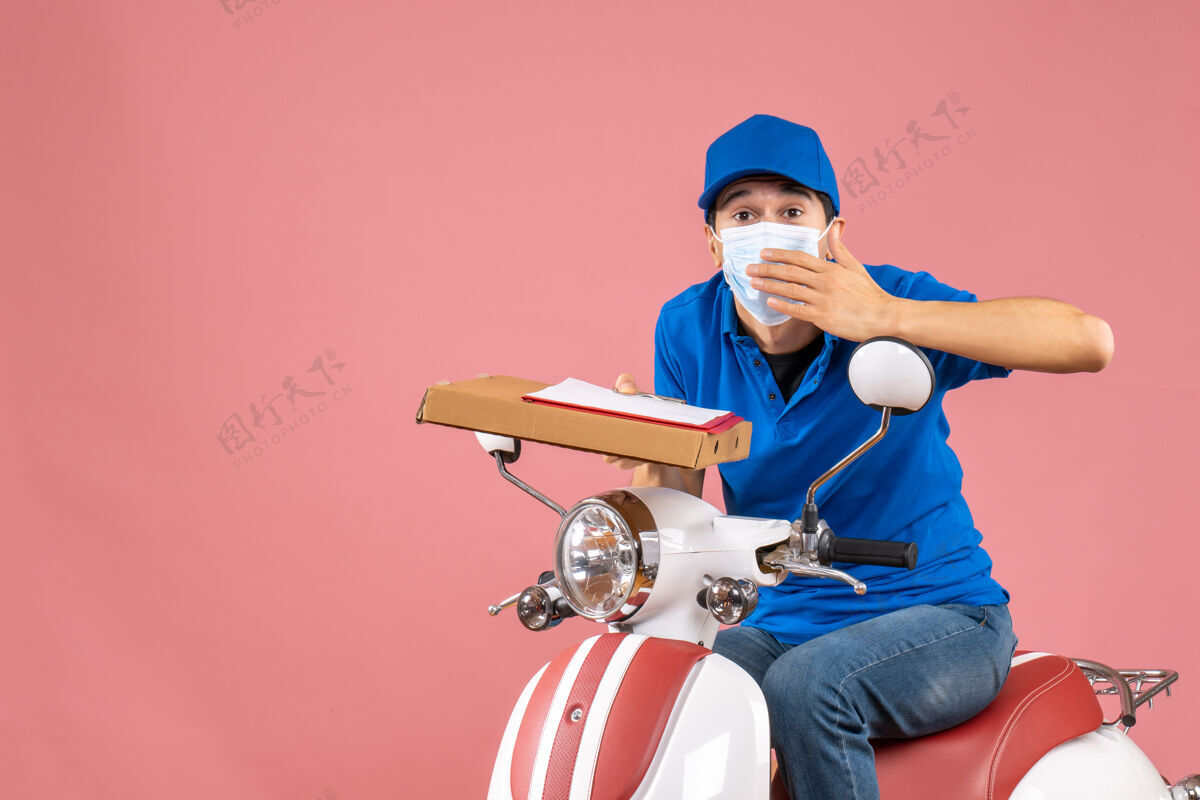 文件戴着面具戴着帽子坐在滑板车上拿着桃色背景文件的男性送货员的俯视图背景桃交付人