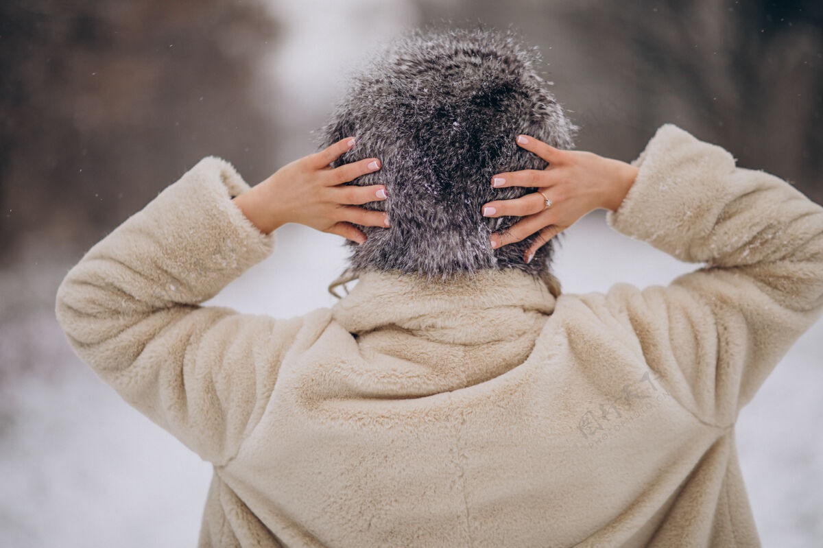 毛衣女人从后面摆姿势 在冬季公园散步美丽帽子自然