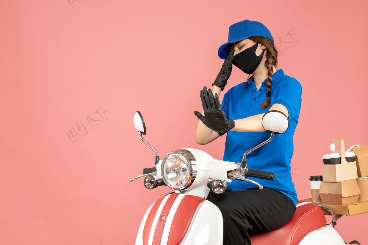 人前视图疲惫的快递女孩戴着医用面罩和手套坐在滑板车上传递粉彩桃背景的命令医疗面具摩托车