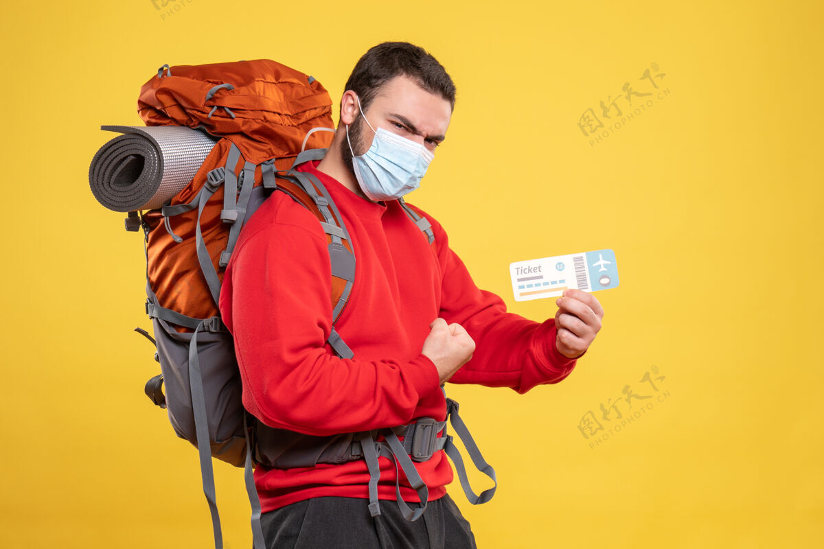 黄色前视图自豪的旅客家伙戴着医疗面具和背包 并显示在黄色背景票男性医疗前面