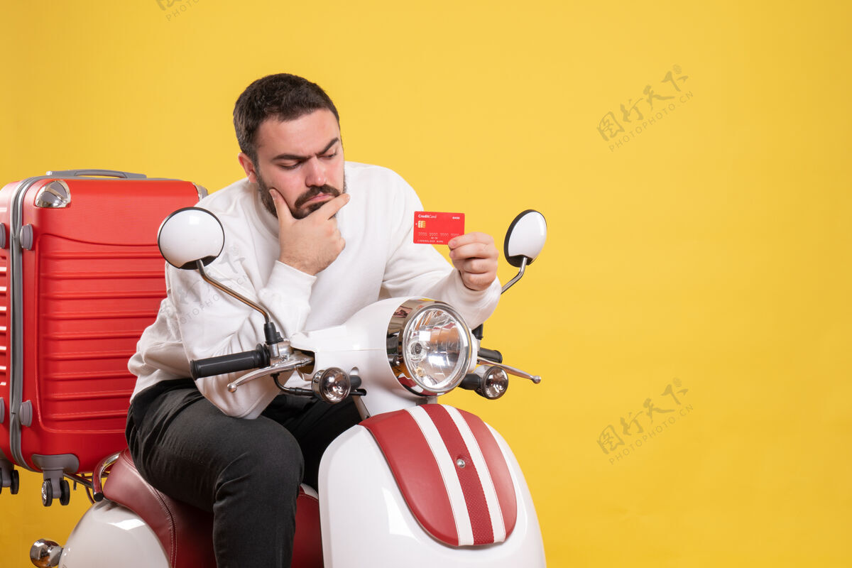 运动员旅行理念 年轻人坐在摩托车上 提着手提箱 手里拿着黄色的银行卡黄色旅行银行
