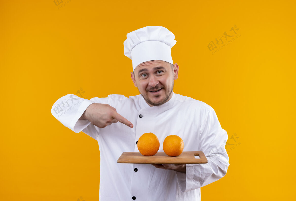 印象穿着厨师制服的年轻帅哥拿着砧板 上面放着橘子 指着隔离在橘色墙上的橘子年轻厨师橙色