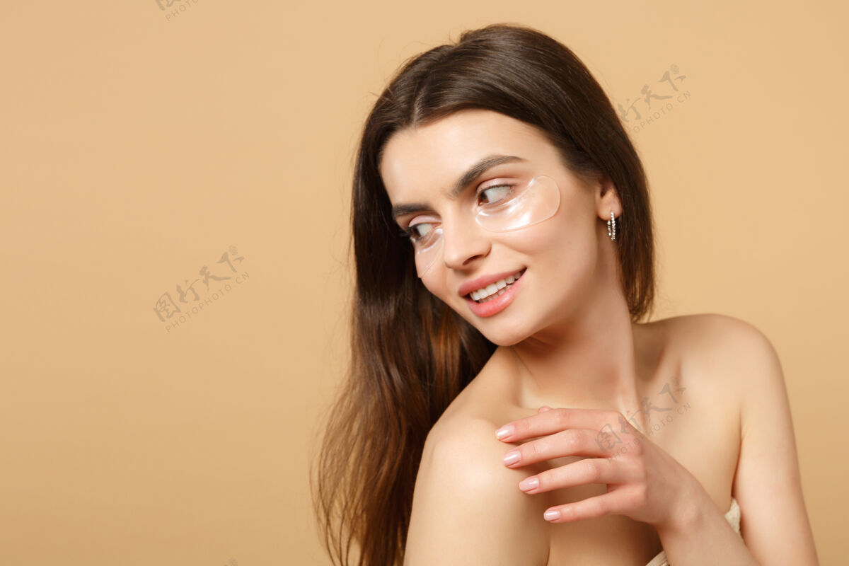 美丽近距离拍摄完美皮肤的半裸女人 在米色粉彩墙上隔离眼睛下的裸妆贴片胶原蛋白新鲜肿胀