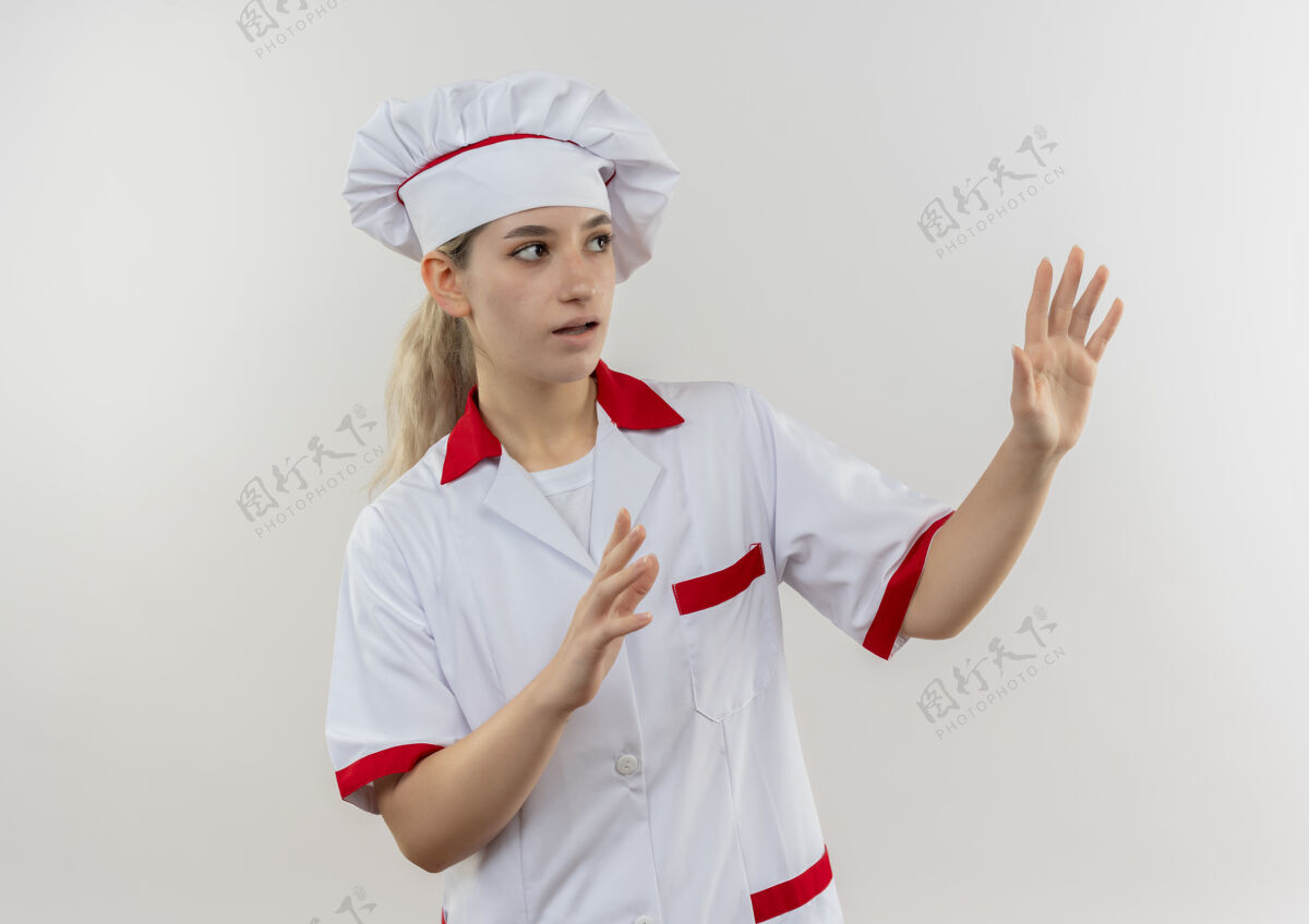 提高年轻漂亮的厨师穿着厨师制服 站在白色的墙壁上 一边看着一边举手 给人留下了深刻的印象印象壁板手