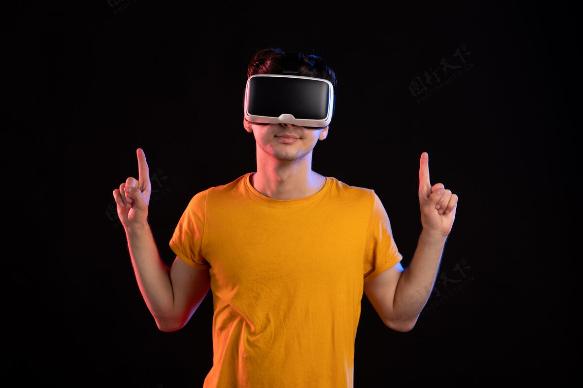 视觉在黑暗的墙上戴着虚拟现实耳机的年轻人的正视图游戏正面年轻人