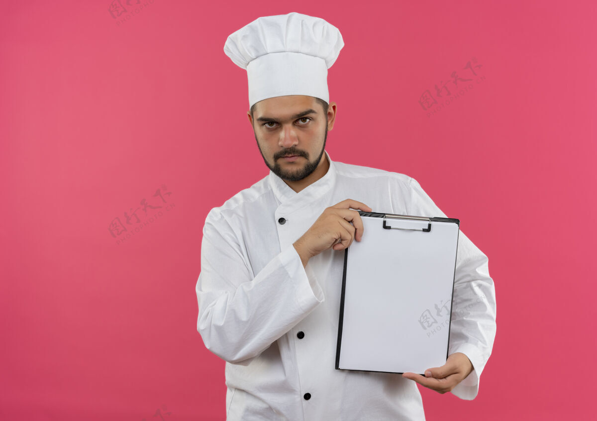 年轻自信的年轻男性厨师身着厨师制服 在粉色墙壁上展示独立的剪贴板 并留有复印空间制服自信展示