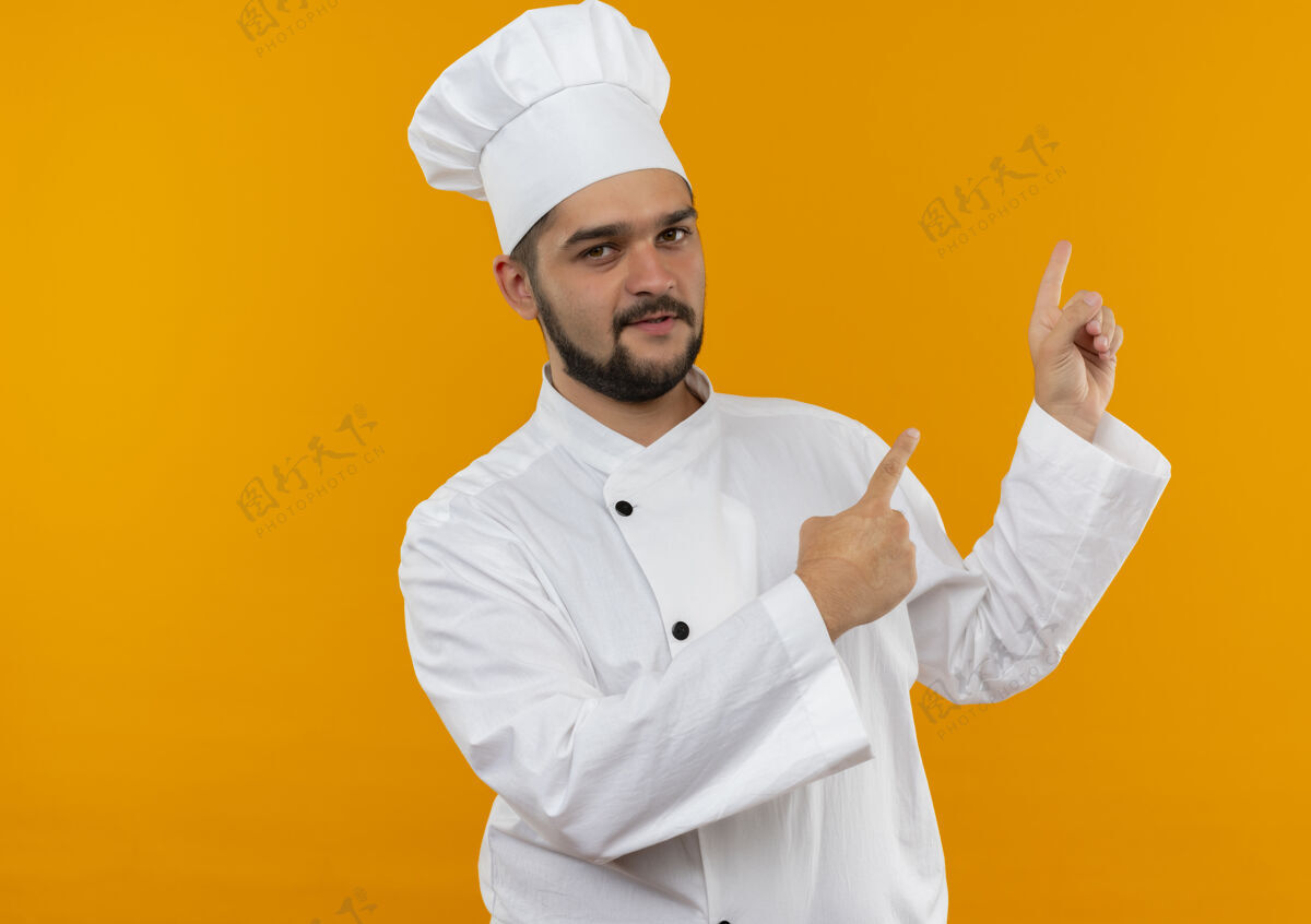 指点自信的年轻男性厨师 身着厨师制服 在橙色的墙壁上指着孤立的复制空间自信烹饪年轻