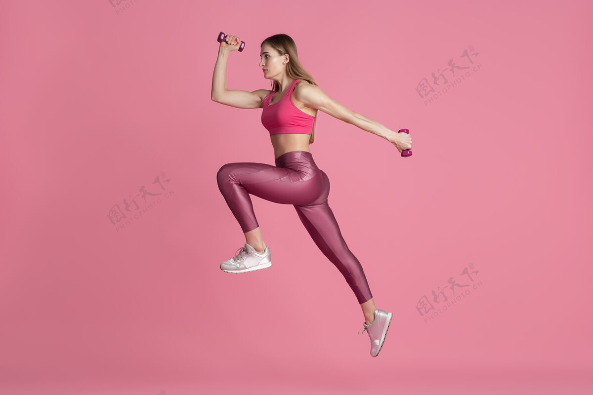 强壮在跳跃 飞行美丽的年轻女运动员在工作室练习 单色粉红色肖像健康运动员护理