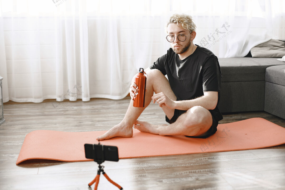 男性健身教练或视频博主在做伸展运动这名男子正在家里用智能手机摄像头拍摄自己沟通伸展运动