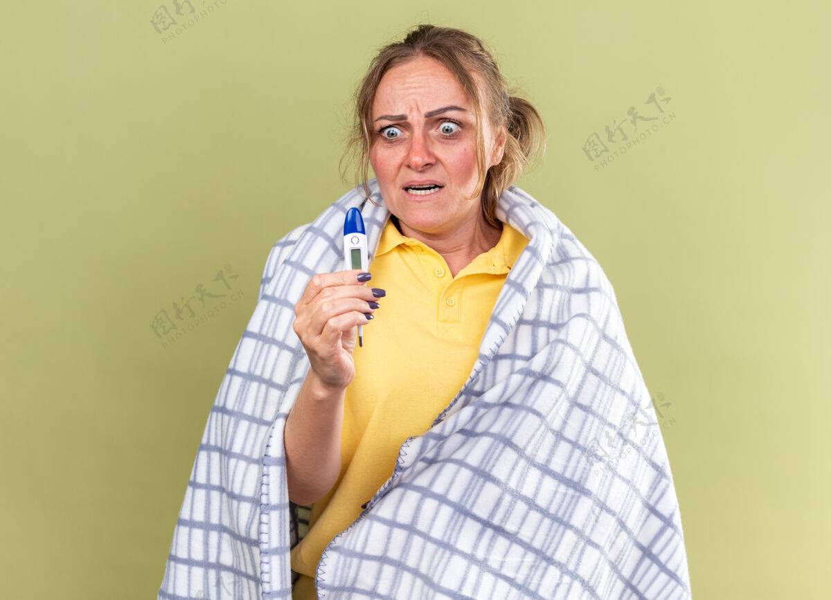感觉不健康的女人裹在毯子里 感觉很可怕 患流感 感冒 拿着温度计站在绿色的墙上 看起来很害怕害怕流感不健康