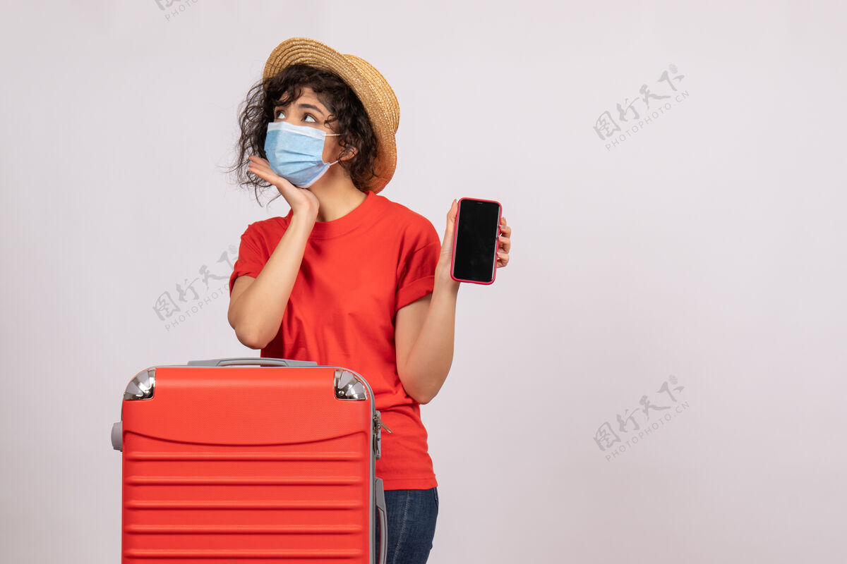 成人正面图年轻女性戴着红包 戴着口罩 手持手机 背景是白色的太阳冠状病毒大流行假期旅游病毒颜色病毒人面具