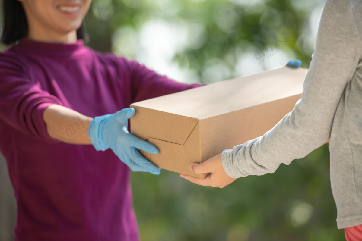 距离来自送货服务部的亚洲女士穿着紫色t恤 送货员的肖像拿着纸板箱包裹站在家门口送货上门购物理念持有运费订单