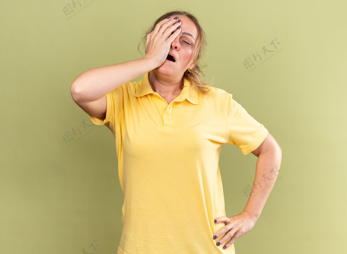 女人穿着黄色衬衫的不健康妇女站在绿色墙壁上 感觉不舒服 摸了摸额头 头晕 感冒头晕站立不适