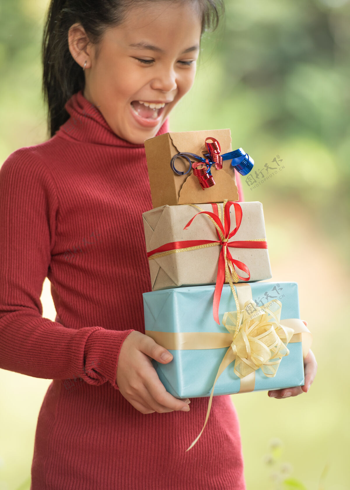 女孩圣诞快乐微笑的小女孩与礼品盒的肖像画在一棵绿色的树枝旁绿色的树叶从自然森林的背景中突出工艺自然树叶