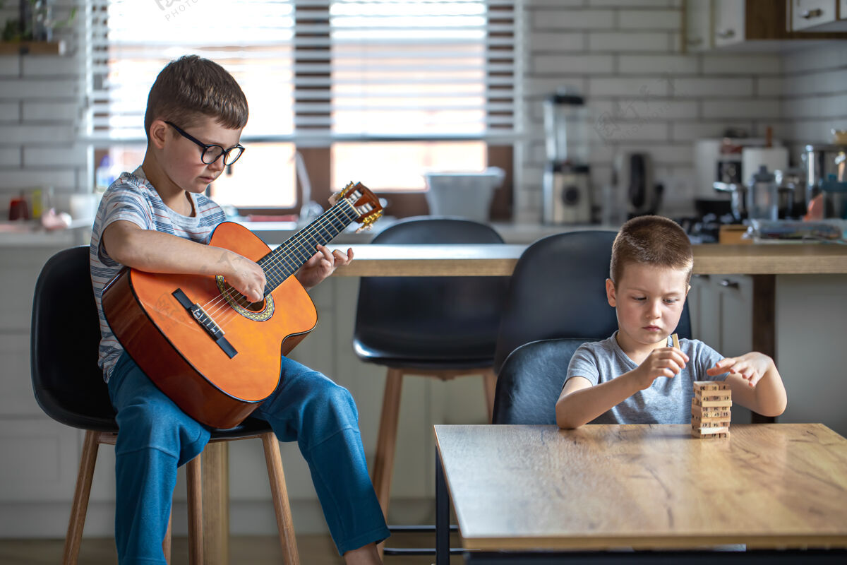音乐一个小男孩弹吉他 他的哥哥在家的桌子旁用木块搭建了一个炮塔发展玩建筑