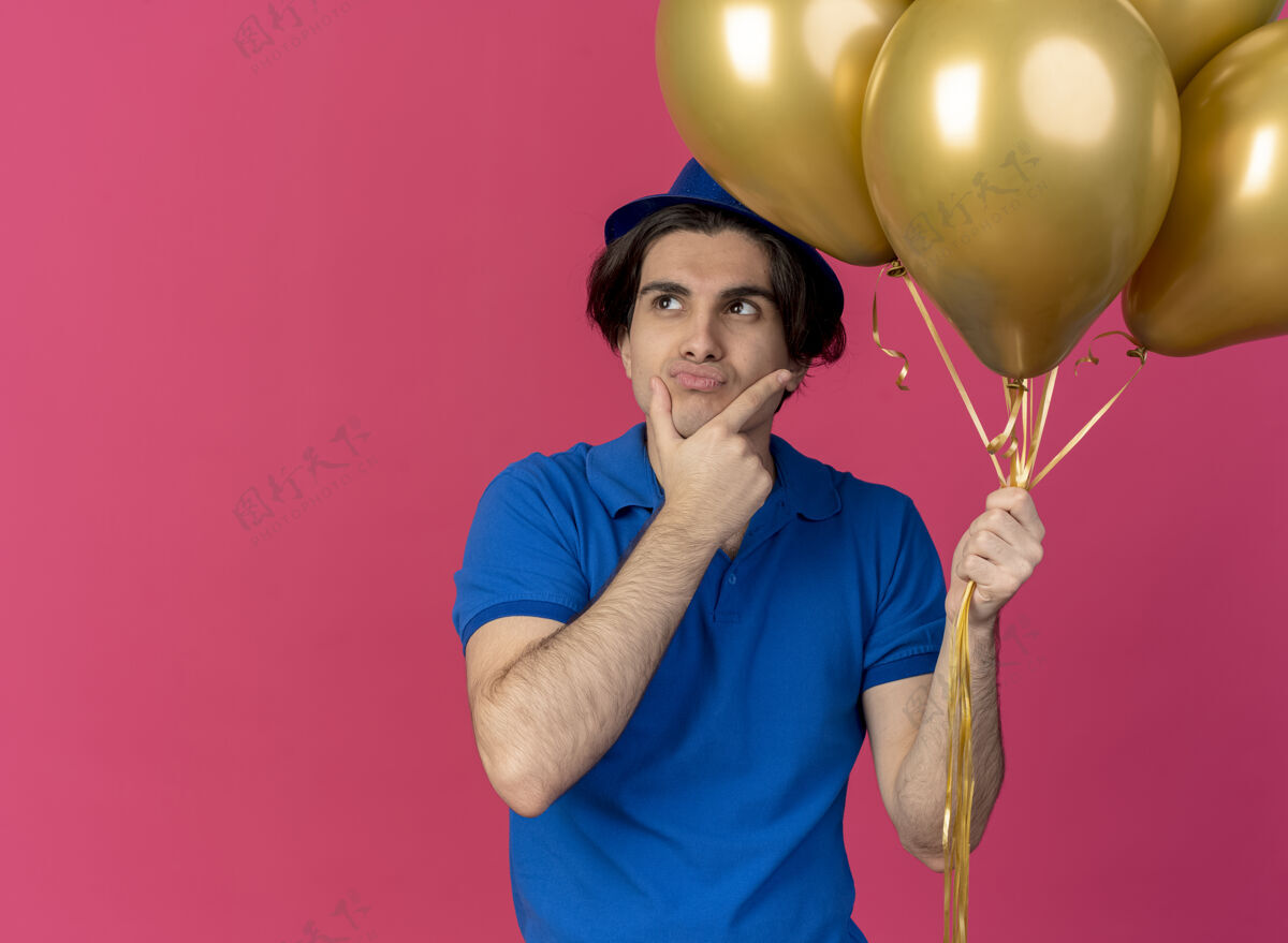 蓝色迷茫英俊的白人男子戴着蓝色派对帽手持氦气球把手放在下巴上手空格复制