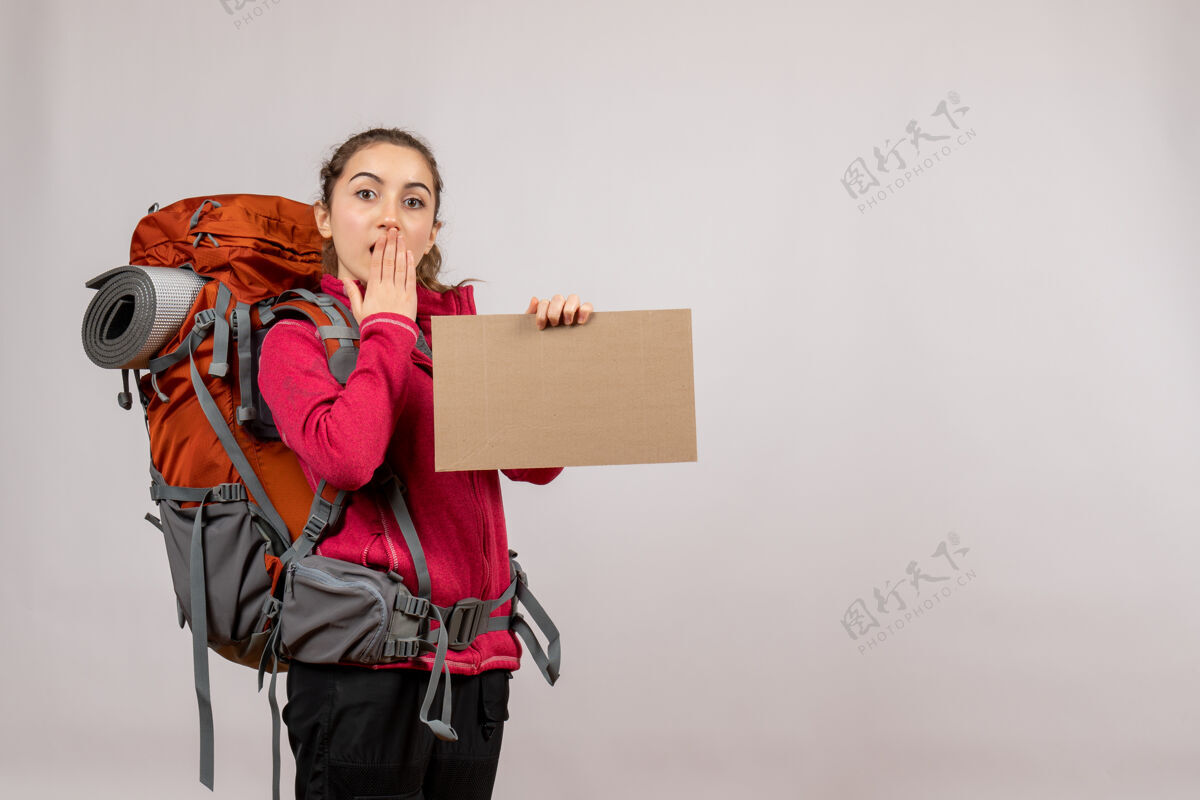 背包年轻的旅行者带着一个大背包 手里拿着灰色的纸板女士人肖像