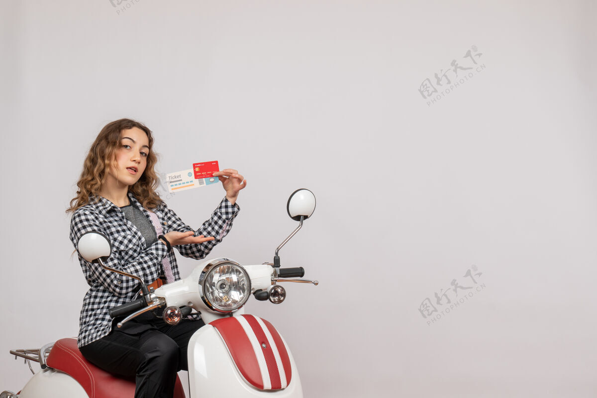 摩托车骑着轻便摩托车的漂亮姑娘 手里拿着灰色的车票和卡车辆灰色坐着