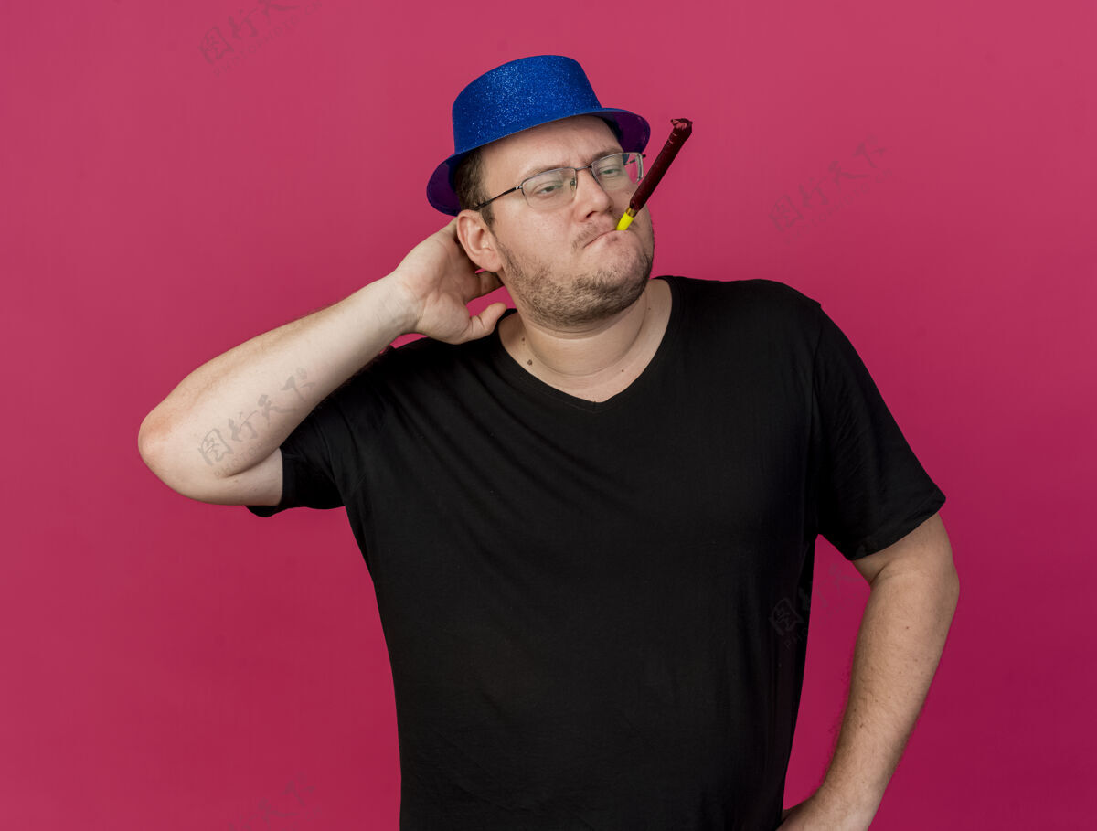 吹自信的成年斯拉夫人戴着眼镜 戴着蓝色派对帽 手放在头上吹派对哨子复制成人手