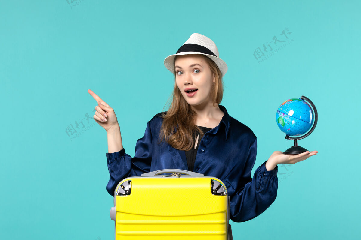 地球仪前视图年轻女子拿着地球仪 在蓝色背景上准备度假女性度假旅行海上飞机欢呼旅程年轻女子