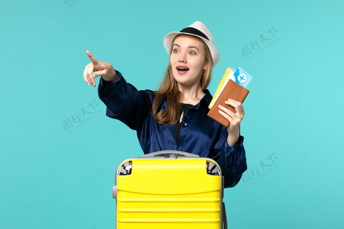 年轻女子前视图年轻女子拿着机票 准备在蓝色背景下旅行海上度假旅行旅行准备成人