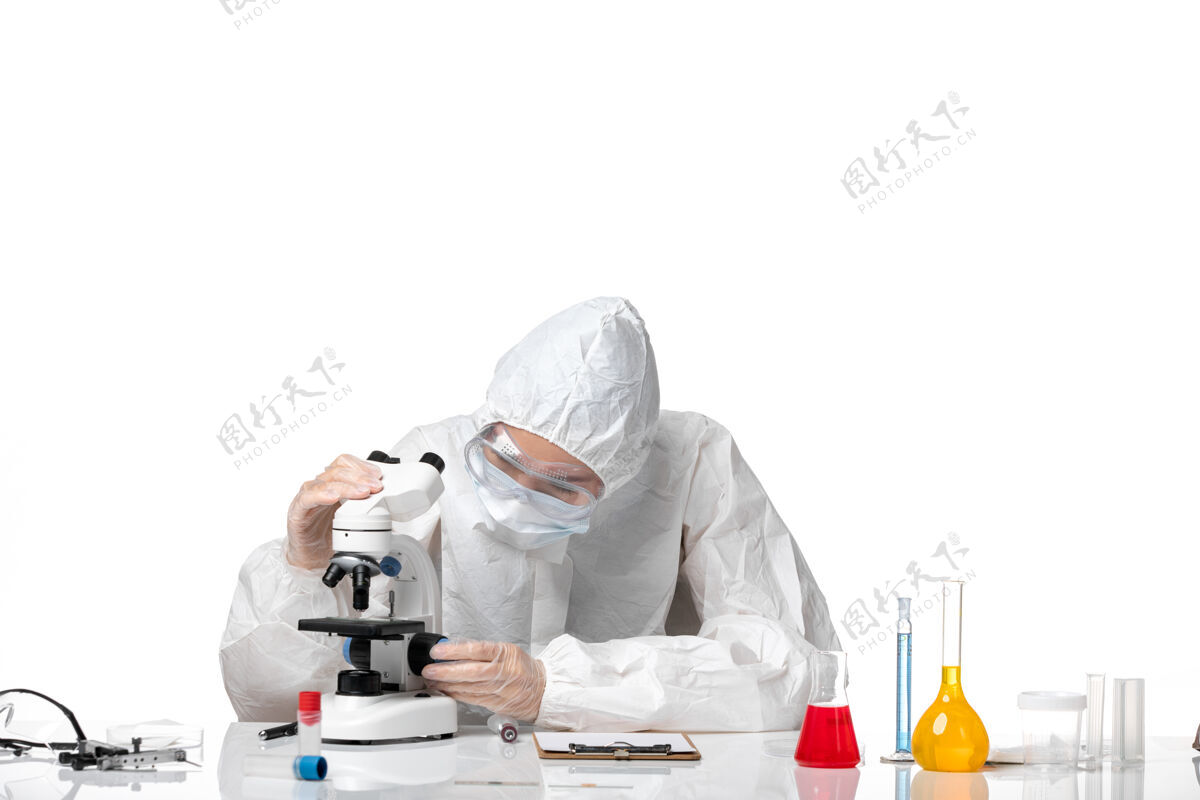 病毒正面图年轻女医生穿着白色防护服 戴着口罩 由于科维德正在用显微镜观察白色背景病毒大流行飞溅的科维德-防护显微镜专业