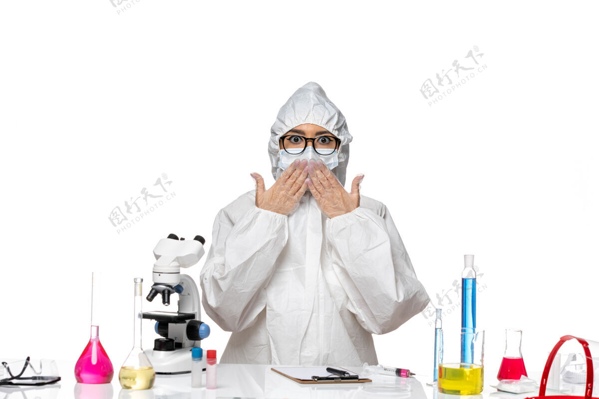 神秘正面图年轻的女化学家穿着特殊的防护服 坐在桌子前 用白色背景的解决方案对病毒实验室的covid健康化学特殊人男性