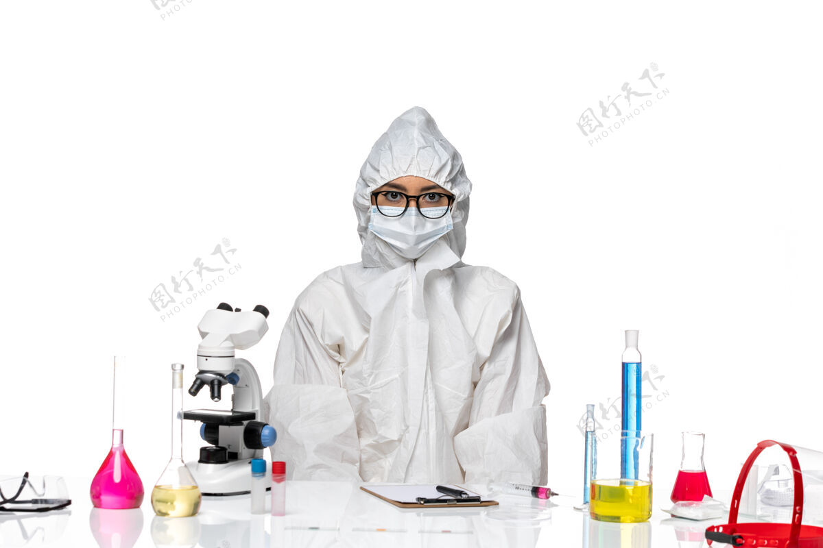 外套前视图年轻的女化学家穿着特殊的防护服 正坐在白色背景上 解决方案实验室冠状病毒化学健康特殊套装坐姿