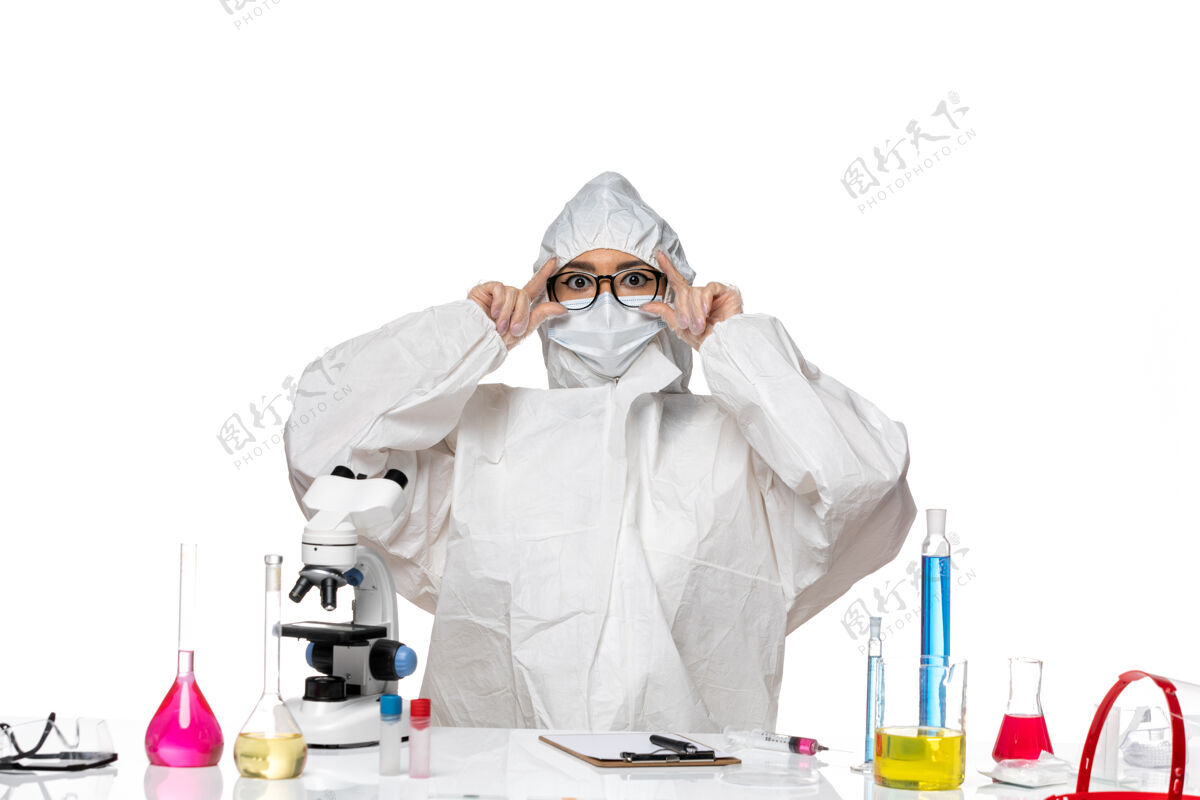 防护正面图穿着特殊防护服的年轻女化学家坐在桌子前 白色办公桌上的解决方案病毒实验室可维健康化学坐姿桌子专业
