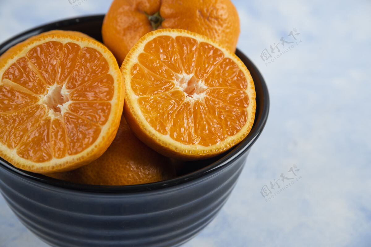 多汁特写的黑色碗充满了整个或一半削减柑桔柑橘碗餐桌