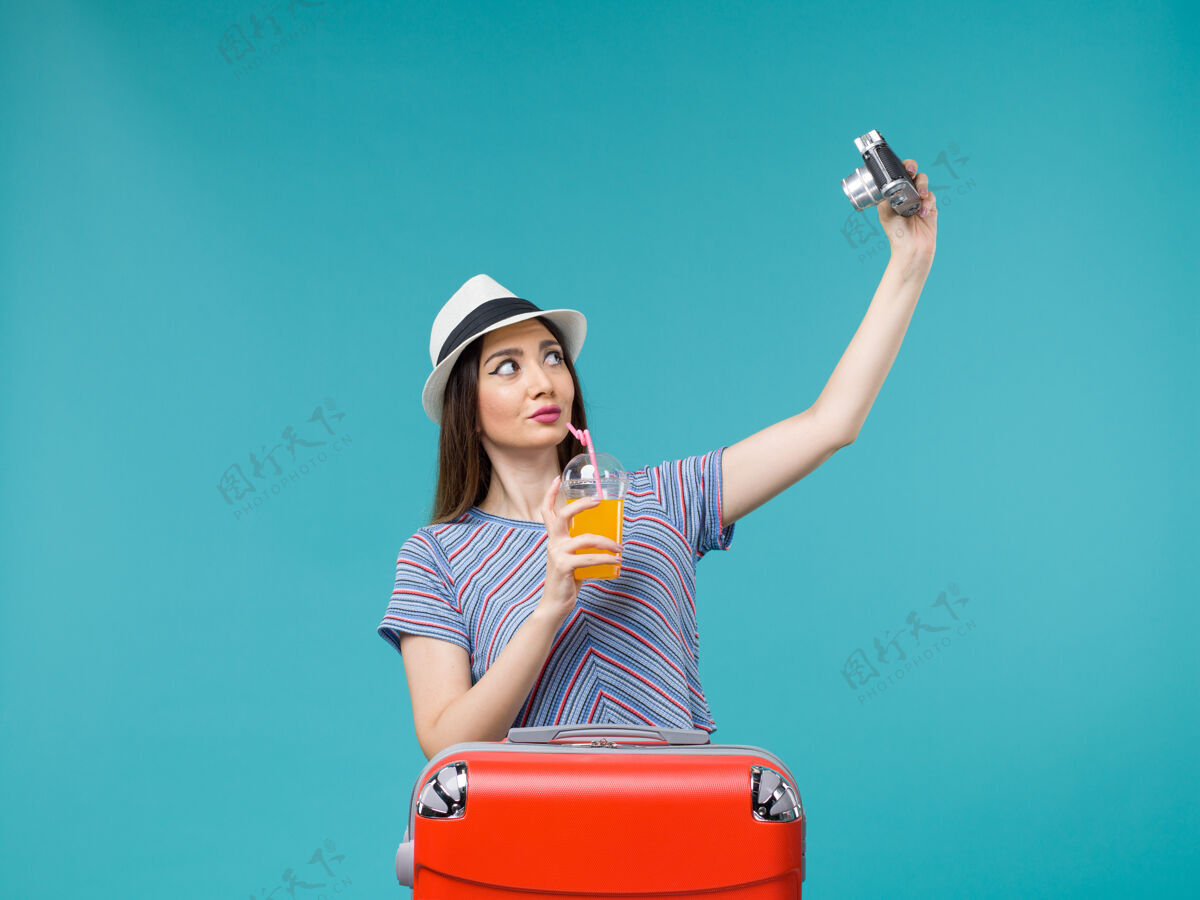 果汁正面图：度假中的女人拿着果汁和相机在蓝色背景上拍照航行暑假海上旅行人航行美丽