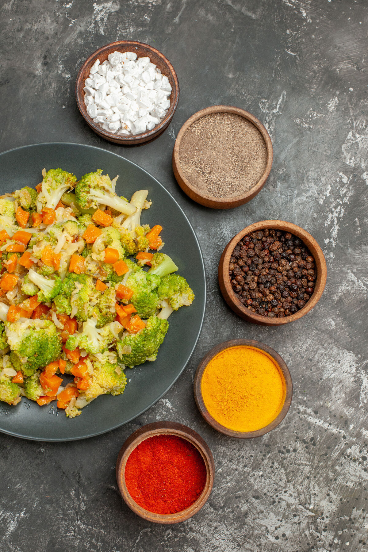 食物黑色盘子上有花椰菜和胡萝卜 灰色桌子上有香料的蔬菜餐的垂直视图洋葱胡萝卜烹饪