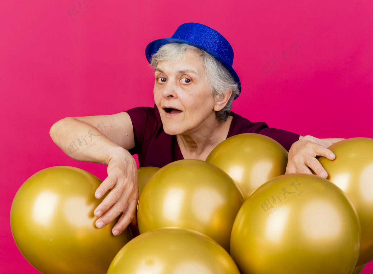 聚会快乐的老妇人戴着聚会帽站在粉红色的氦气球后面帽子穿上粉色
